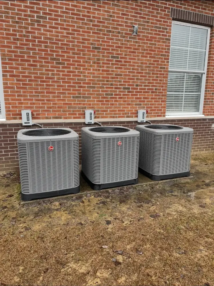 Three outdoor HVAC condenser units installed beside a brick building